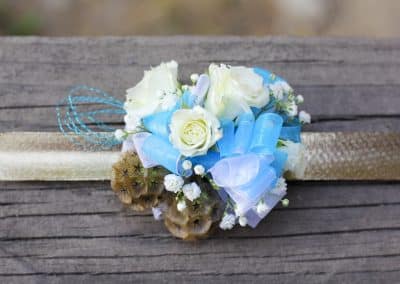 Corsage on a slap band that includes white roses, scabiosa, blue and white ribbon.