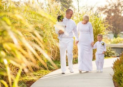 Family dressed in white while baby girl wears flower crown and toddler boy with boutonniere.