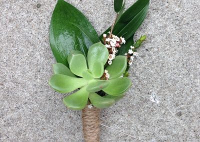 Boutonniere that includes a succulent and greenery wrapped in jute.