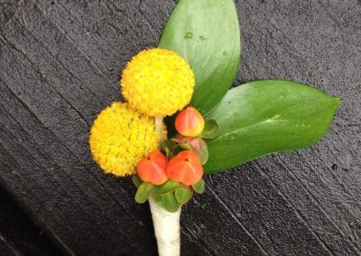 Boutonnière that includes yellow billy balls, coral hypericum berries, and greenery.