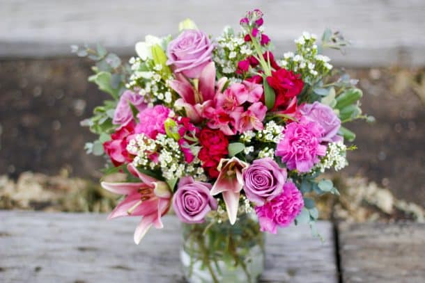 Vased arrangement that includes pink lilies, lavender roses, wax flowers, and eucalyptus.