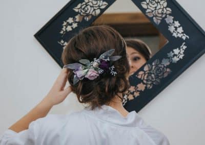 Bride wearing floral clip that includes silver eucalyptus, purple roses, purple lisianthus, and purple carnations.