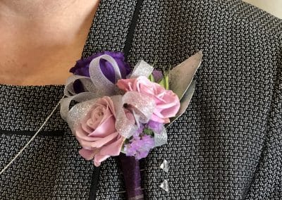 Mother's chest corsage that includes silver ribbon, lavender mini roses, purple lisianthus, purple statice, silver eucalyptus, and is wrapped in plum ribbon.