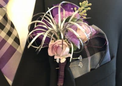 Groom's boutonniere that includes purple roses and a silver air plant.