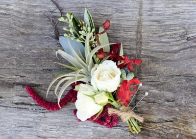 Grooms boutonniere that includes ivory mini roses, eucalyptus, airplants, burgundy orchids, burgundy amaranthus, and wrapped with twine.