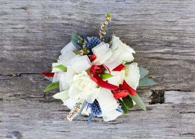 Mother's wrist corsage that includes ivory ribbon, ivory mini roses, thistle, burgundy orchids, and eucalyptus.