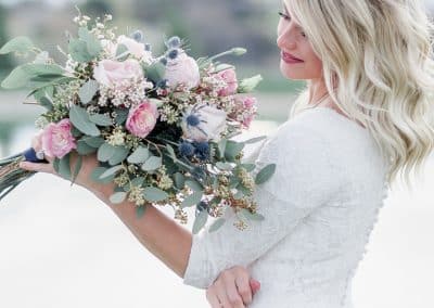 Beautiful bride holding wedding bouquet with pink roses, thistle, and eucalyptus.