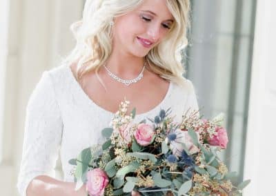 Beautiful bride holding wedding bouquet with pink roses, thistle, and eucalyptus.